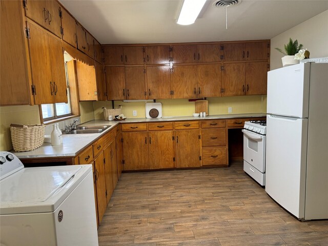 kitchen with white appliances, sink, washing machine and dryer, and light hardwood / wood-style flooring