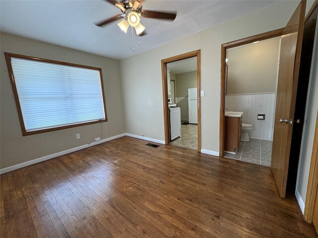 unfurnished bedroom with white fridge, hardwood / wood-style floors, connected bathroom, ceiling fan, and wooden walls