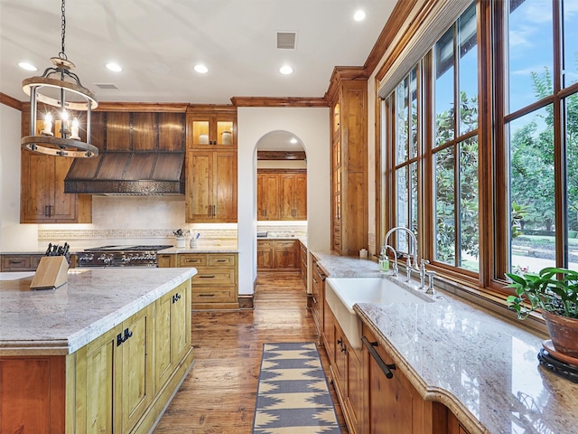 kitchen with light stone countertops, sink, backsplash, decorative light fixtures, and ornamental molding