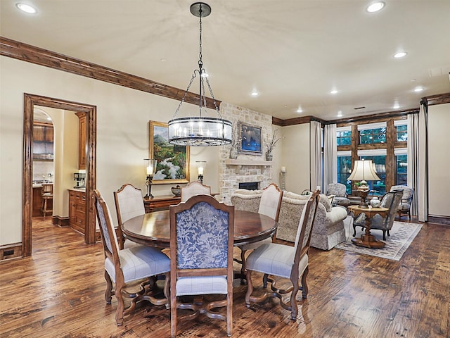 dining area featuring ornamental molding, a stone fireplace, and dark wood-type flooring