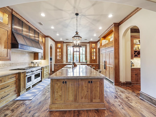 kitchen featuring light stone countertops, premium appliances, crown molding, pendant lighting, and an island with sink