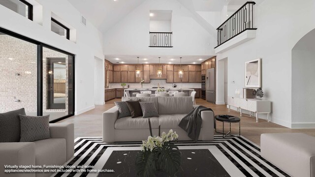 kitchen with a towering ceiling, pendant lighting, an island with sink, backsplash, and light hardwood / wood-style floors