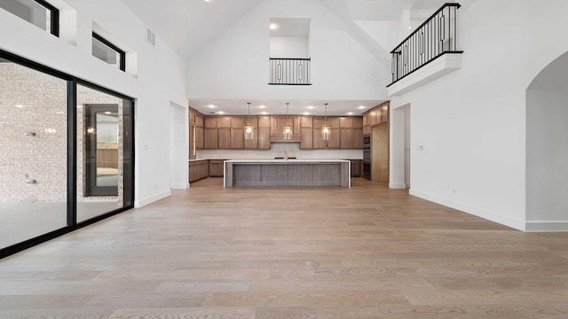 kitchen with a high ceiling, a kitchen island with sink, light hardwood / wood-style flooring, and decorative light fixtures