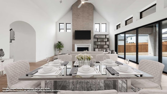 dining space with a large fireplace, a healthy amount of sunlight, high vaulted ceiling, and wood-type flooring