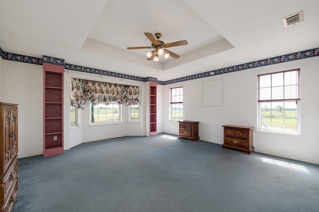 interior space featuring ceiling fan, dark colored carpet, a tray ceiling, and a textured ceiling