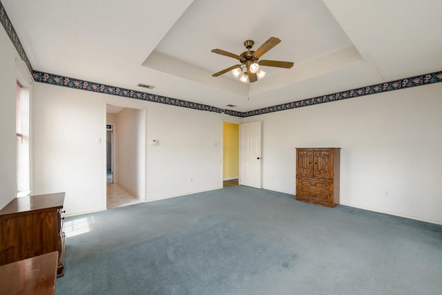 carpeted spare room featuring a healthy amount of sunlight, ceiling fan, and a tray ceiling