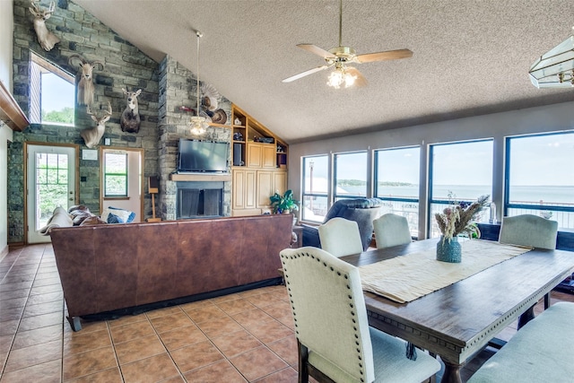 tiled dining space featuring lofted ceiling, a textured ceiling, a stone fireplace, and ceiling fan