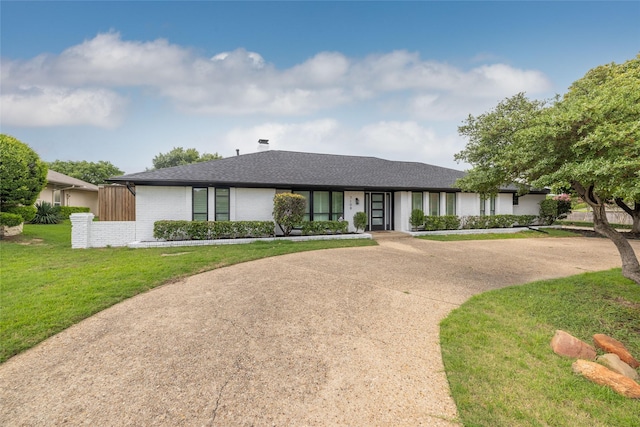 ranch-style home featuring concrete driveway, a front lawn, roof with shingles, and brick siding