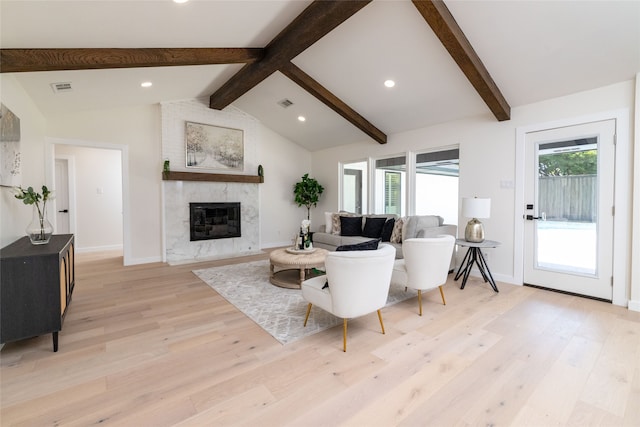 living room featuring vaulted ceiling with beams, a healthy amount of sunlight, a premium fireplace, and light hardwood / wood-style flooring