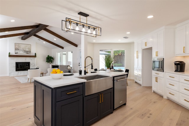 kitchen featuring a high end fireplace, white cabinets, light hardwood / wood-style flooring, an island with sink, and appliances with stainless steel finishes