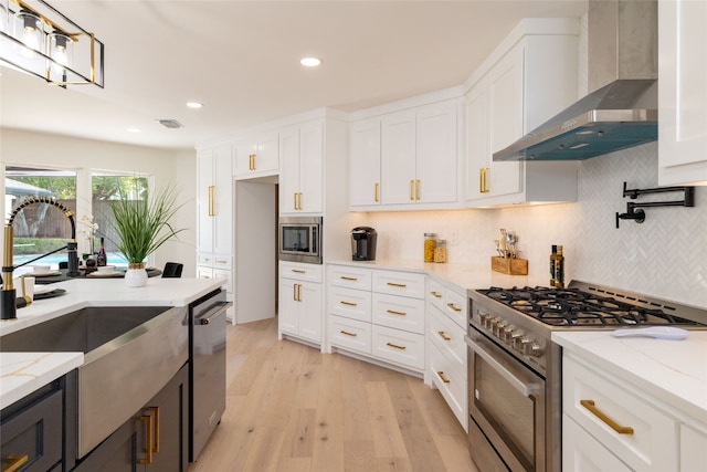 kitchen featuring light stone counters, wall chimney exhaust hood, stainless steel appliances, sink, and white cabinets