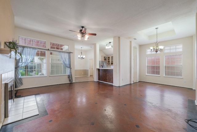 unfurnished living room featuring dark tile patterned flooring, ceiling fan with notable chandelier, and a tray ceiling