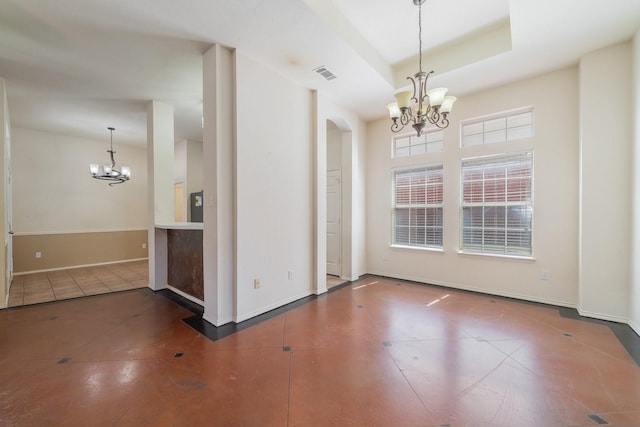 empty room with a raised ceiling, dark tile patterned floors, and an inviting chandelier