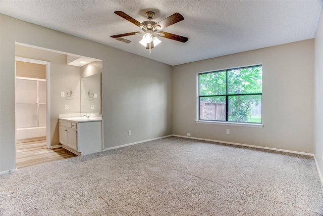 unfurnished bedroom with ceiling fan, sink, ensuite bathroom, light colored carpet, and a textured ceiling