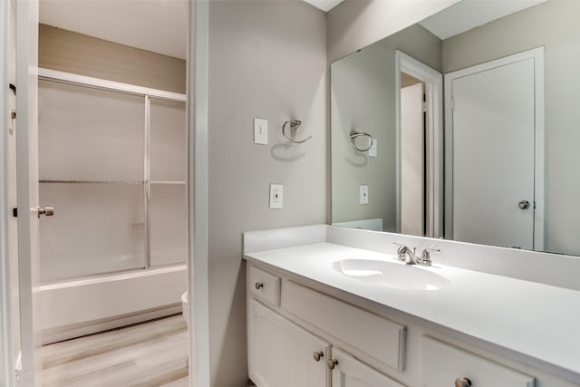 full bathroom featuring hardwood / wood-style floors, vanity, toilet, and bath / shower combo with glass door