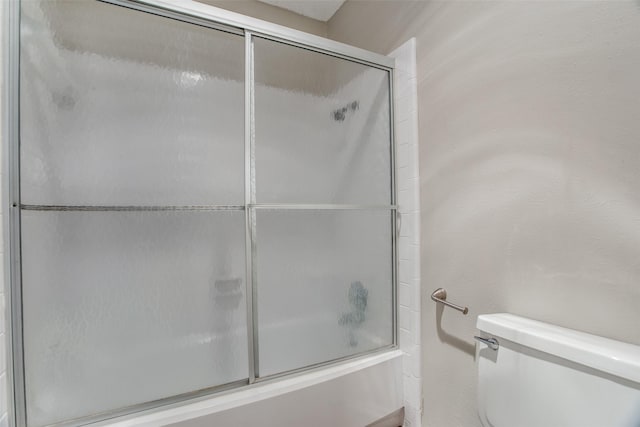 bathroom featuring toilet and bath / shower combo with glass door