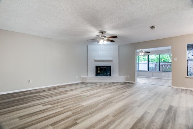 unfurnished living room with a fireplace, ceiling fan, light hardwood / wood-style flooring, and a textured ceiling