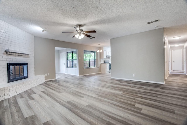 unfurnished living room featuring a fireplace, wood-type flooring, a textured ceiling, and ceiling fan with notable chandelier