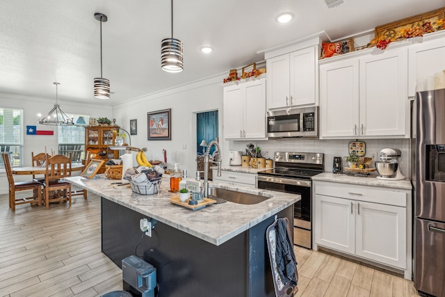 kitchen with decorative light fixtures, stainless steel appliances, backsplash, white cabinetry, and an island with sink