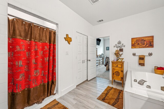 bathroom with a relaxing tiled bath and hardwood / wood-style flooring