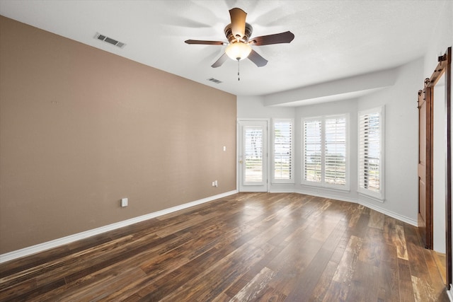 unfurnished bedroom featuring ceiling fan, dark hardwood / wood-style flooring, and a barn door