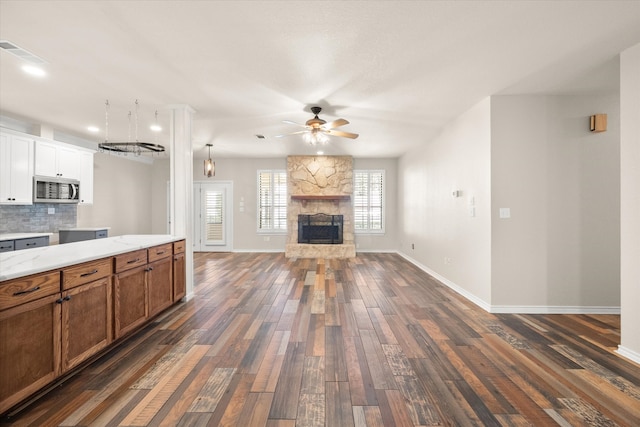 kitchen featuring ceiling fan, decorative backsplash, a stone fireplace, dark hardwood / wood-style flooring, and white cabinets