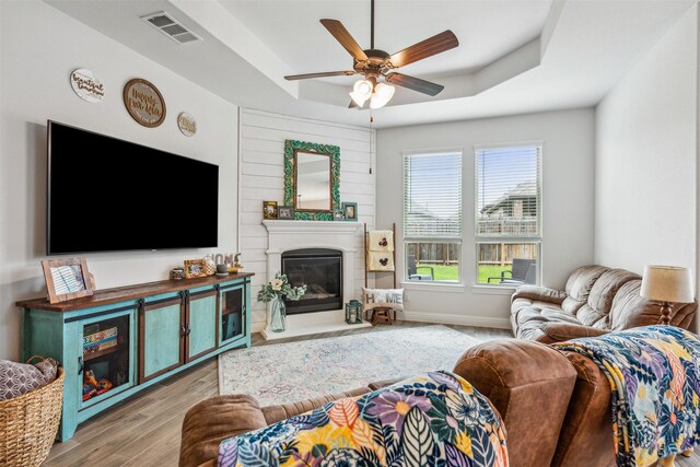 living room featuring ceiling fan, light hardwood / wood-style flooring, and a tray ceiling