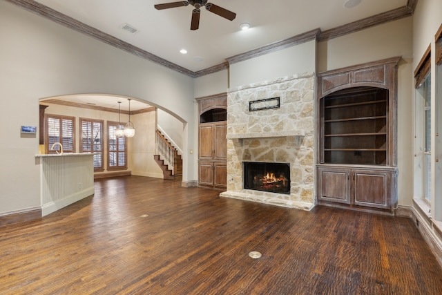 unfurnished living room with a fireplace, dark wood-type flooring, ceiling fan with notable chandelier, and ornamental molding