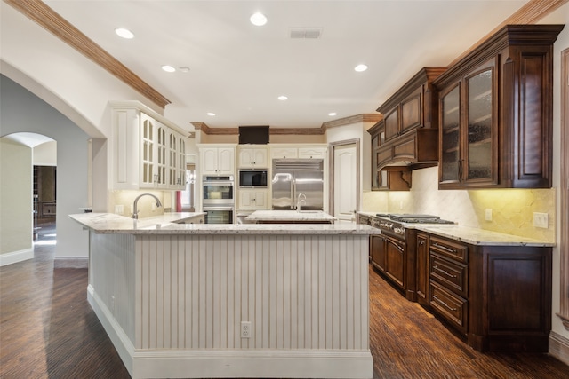 kitchen featuring crown molding, dark wood-type flooring, built in appliances, dark brown cabinetry, and tasteful backsplash