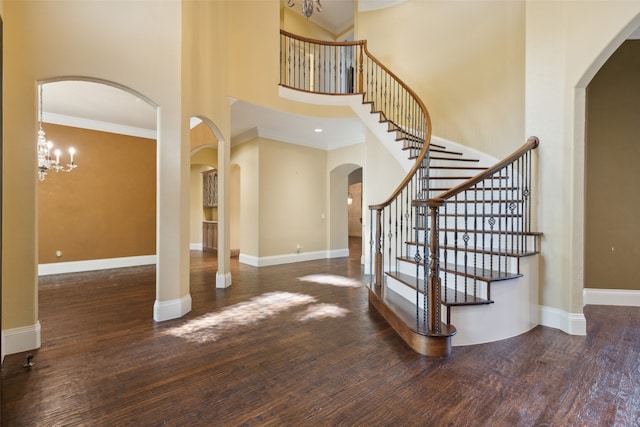 entrance foyer with dark hardwood / wood-style flooring, a towering ceiling, crown molding, and an inviting chandelier