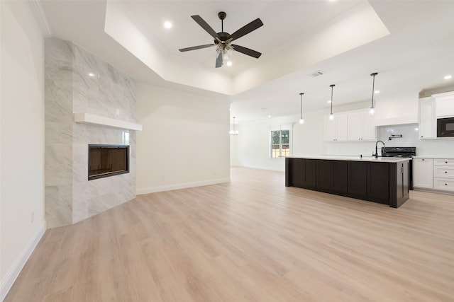 kitchen with light hardwood / wood-style floors, a fireplace, a kitchen island with sink, white cabinets, and pendant lighting