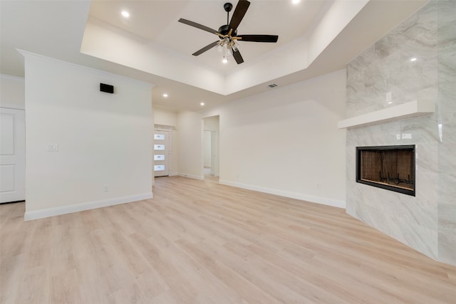 unfurnished living room with ceiling fan, light hardwood / wood-style floors, a tiled fireplace, and a tray ceiling