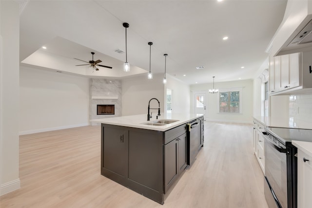 kitchen featuring sink, decorative light fixtures, an island with sink, black electric range, and white cabinets