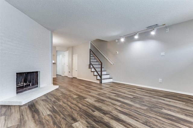 unfurnished living room with track lighting, dark hardwood / wood-style flooring, a brick fireplace, and a textured ceiling