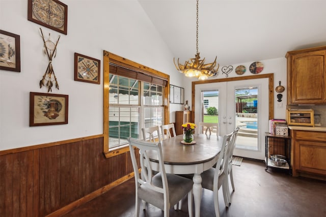 dining area featuring wooden walls, french doors, lofted ceiling, and an inviting chandelier