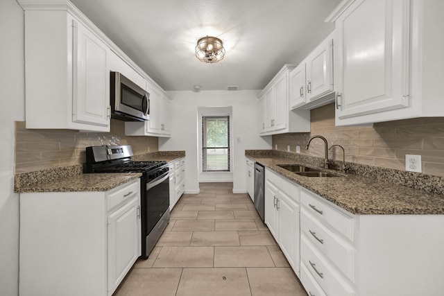 kitchen featuring sink, light tile patterned flooring, dark stone countertops, white cabinets, and appliances with stainless steel finishes