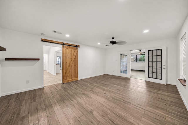 unfurnished living room featuring ceiling fan, a barn door, and wood-type flooring