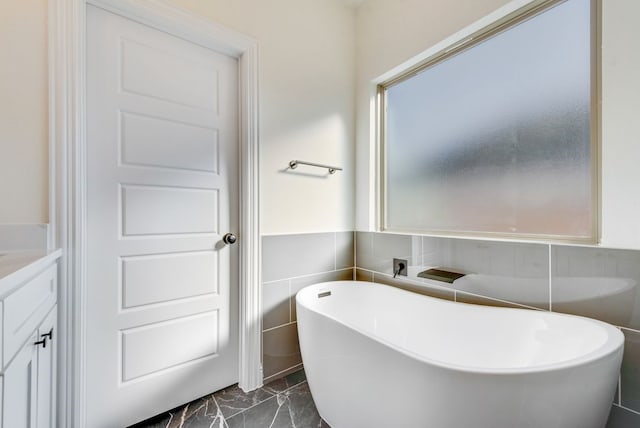 bathroom featuring a tub to relax in, vanity, and tile walls