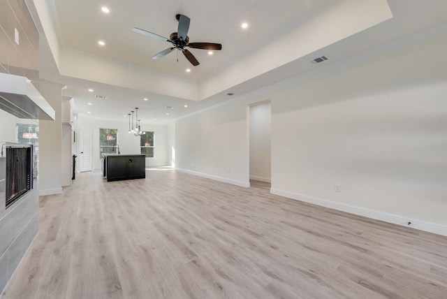 unfurnished living room featuring light wood-type flooring, ceiling fan, and a raised ceiling