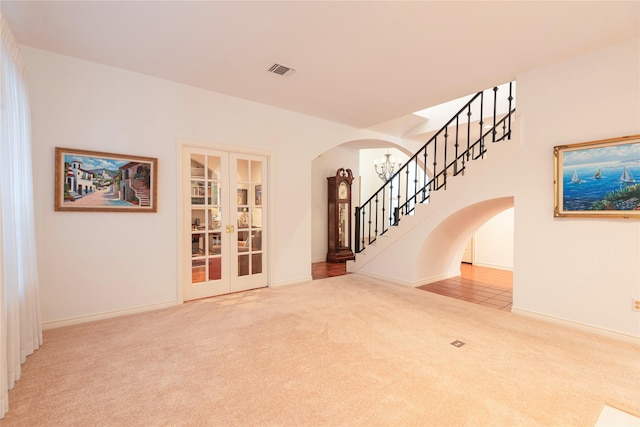 unfurnished living room featuring french doors, carpet floors, and an inviting chandelier