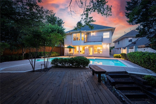 back house at dusk with a balcony and a pool side deck