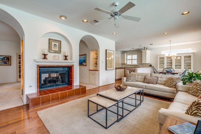 living room with a tile fireplace, light hardwood / wood-style flooring, and ceiling fan with notable chandelier