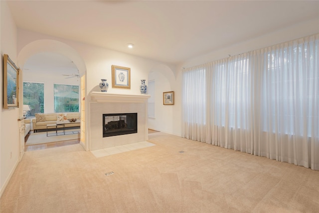 living room featuring light carpet, ceiling fan, and a tiled fireplace