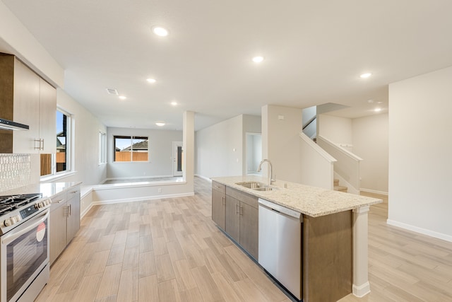 kitchen featuring appliances with stainless steel finishes, light stone countertops, sink, light hardwood / wood-style floors, and a kitchen island with sink