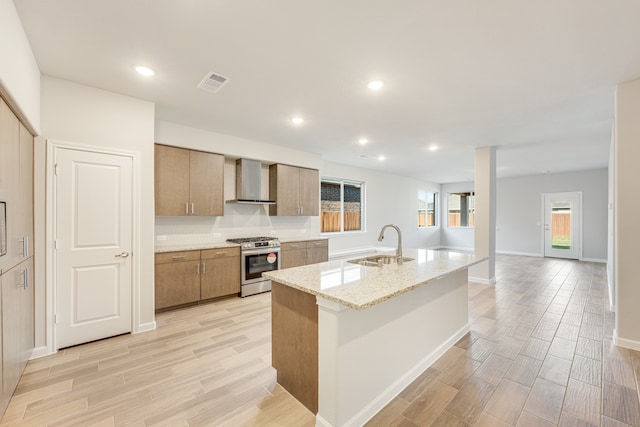 kitchen with stainless steel gas range oven, wall chimney exhaust hood, sink, and light wood-type flooring