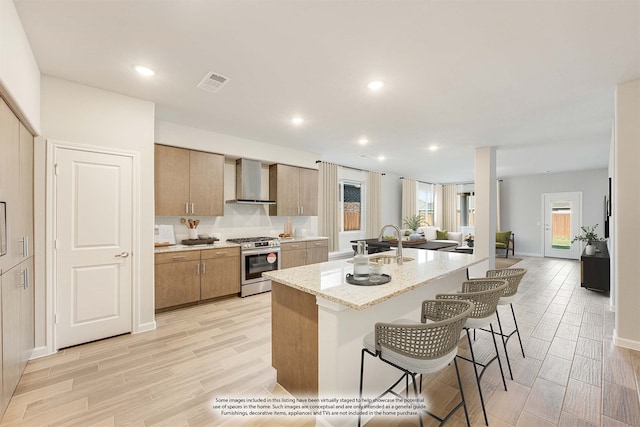 kitchen featuring a kitchen bar, stainless steel range with gas stovetop, a kitchen island with sink, and light hardwood / wood-style floors