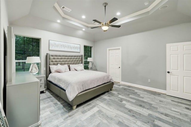 bedroom featuring a raised ceiling, ceiling fan, ornamental molding, and light wood-type flooring