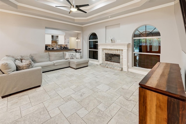 living room featuring a high end fireplace, a raised ceiling, ceiling fan, and crown molding