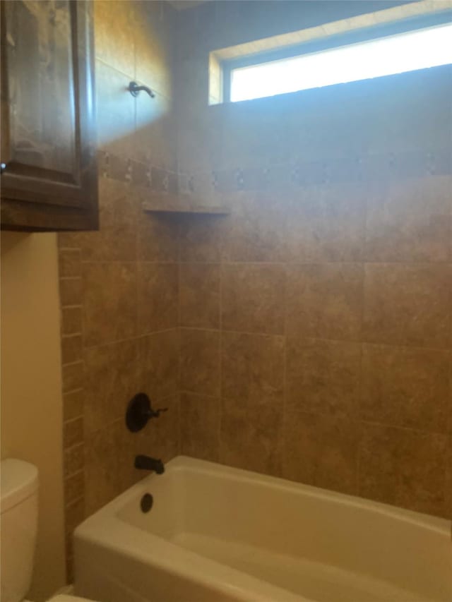 bathroom featuring tiled shower / bath combo and toilet