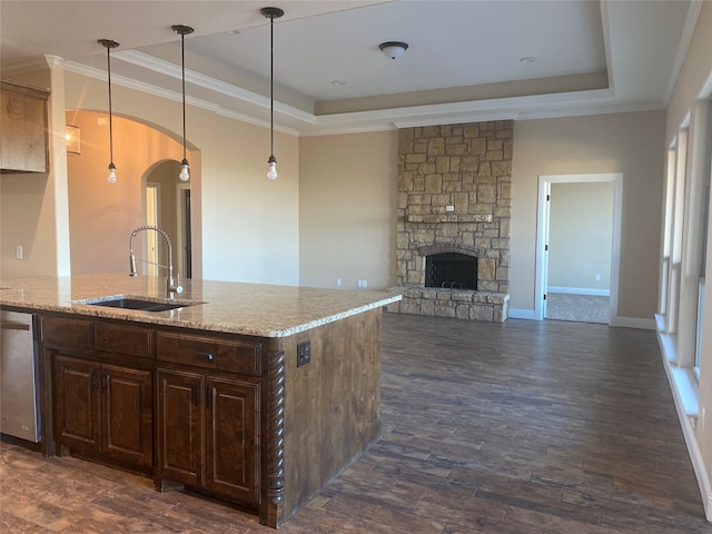 kitchen with decorative light fixtures, a stone fireplace, sink, dishwasher, and a raised ceiling